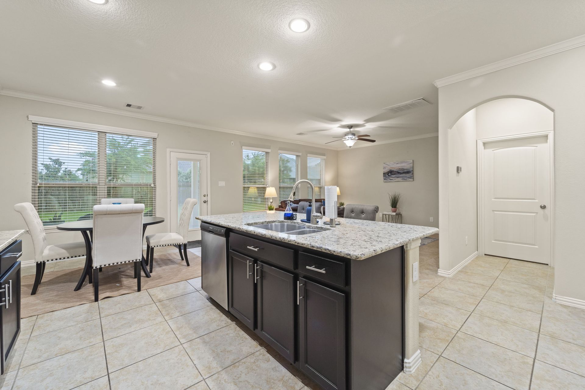 Open-concept kitchen with dark cabinets, granite countertop island, and a dining area with a table and chairs, overlooking a backyard view.