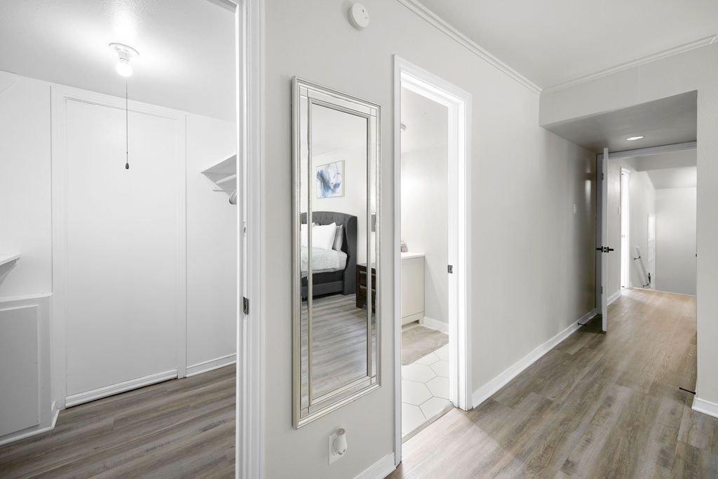 Hallway with gray walls, wood-look flooring, and doors leading to rooms. A decorative mirror hangs on the wall.