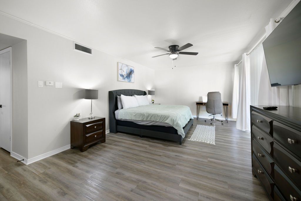 Spacious bedroom with wood-look flooring, a dark bed, nightstand, and dresser. Includes a desk and a ceiling fan.