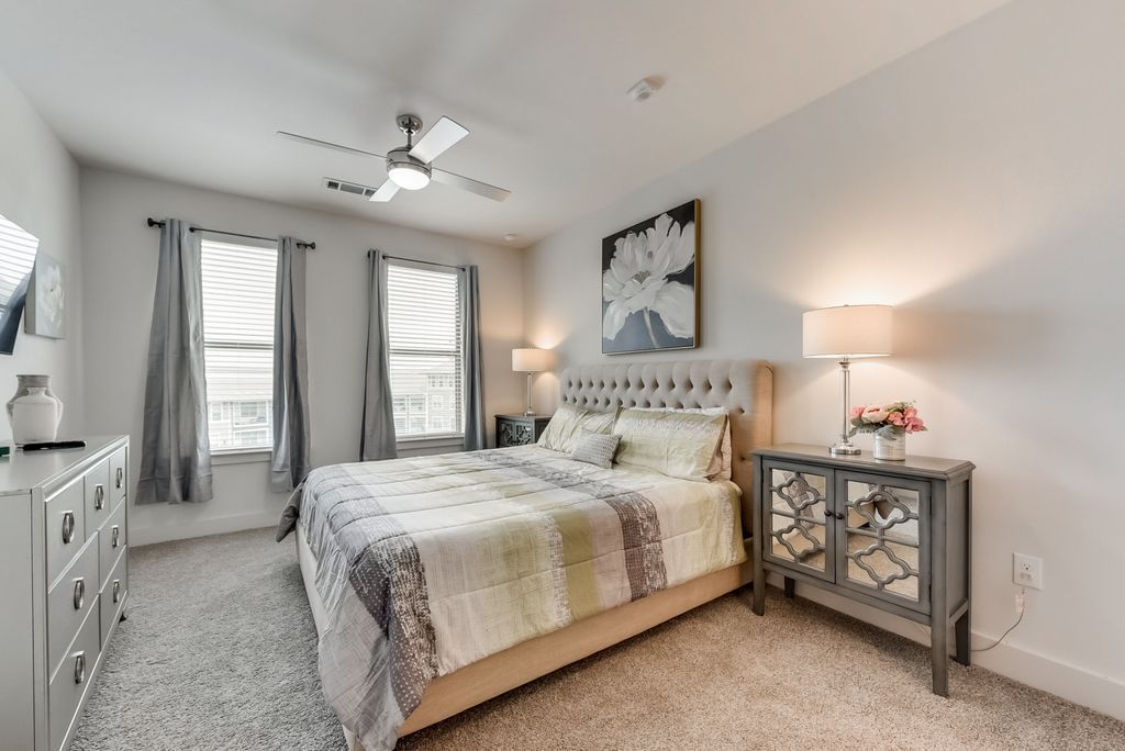 A bedroom with a bed, dresser, and nightstand. The bed has a tufted headboard, and the room is decorated in neutral colors.