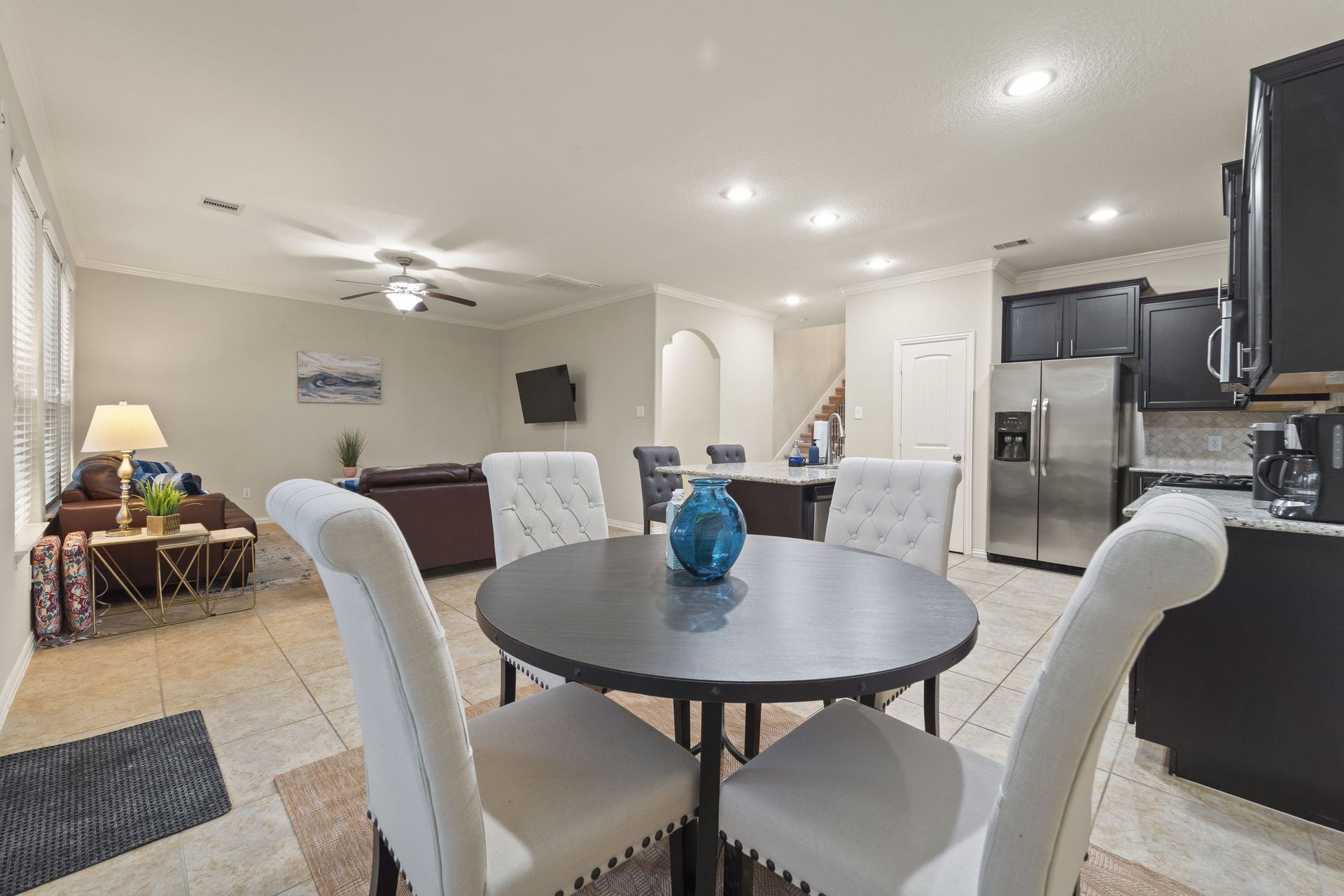 A modern open-concept dining and living area with a round table, chairs, and a view to a kitchen and living room.