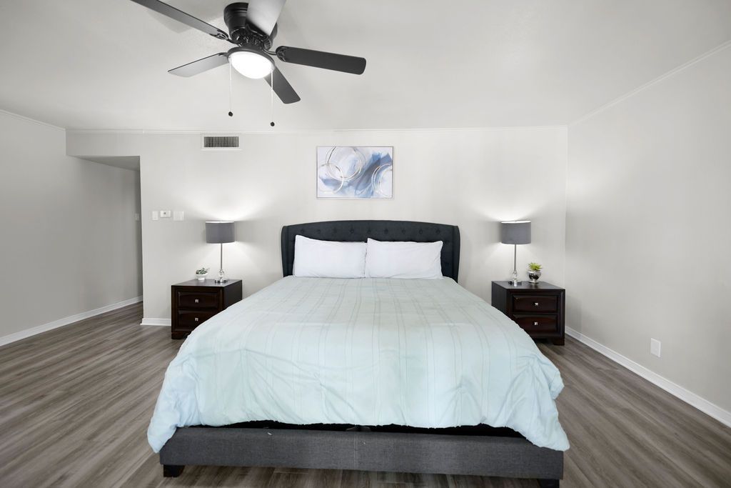 Bedroom with a gray bed, two nightstands with lamps, and a ceiling fan. Light blue bedding and a framed art piece.