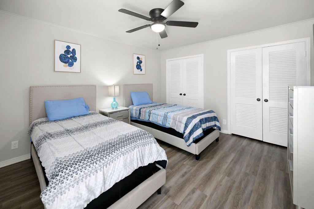Bedroom with two twin beds, gray walls, white closet doors, and a ceiling fan. Beds have blue and white bedding and light gray headboards.