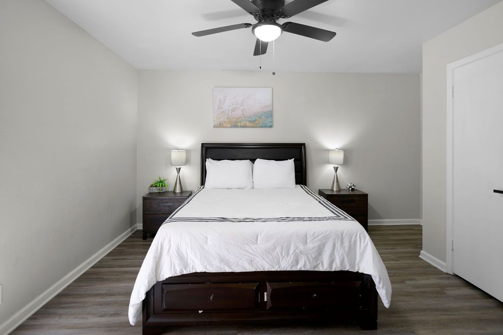 Bedroom with a bed, two nightstands, and a ceiling fan. Light gray walls, dark wood bedframe and furniture, and gray flooring.