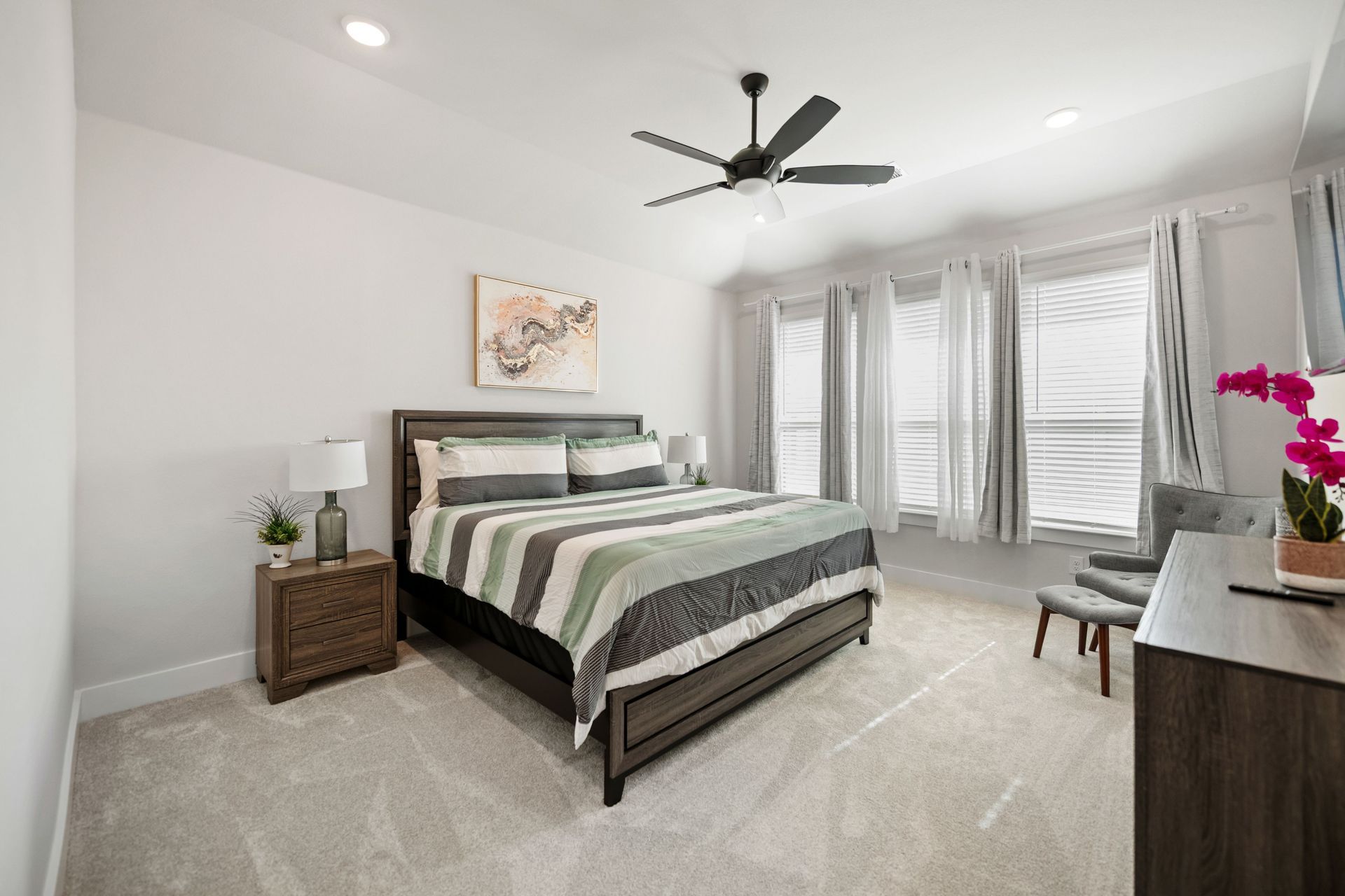 Bedroom with bed, nightstands, windows, chair, and art; neutral colors.