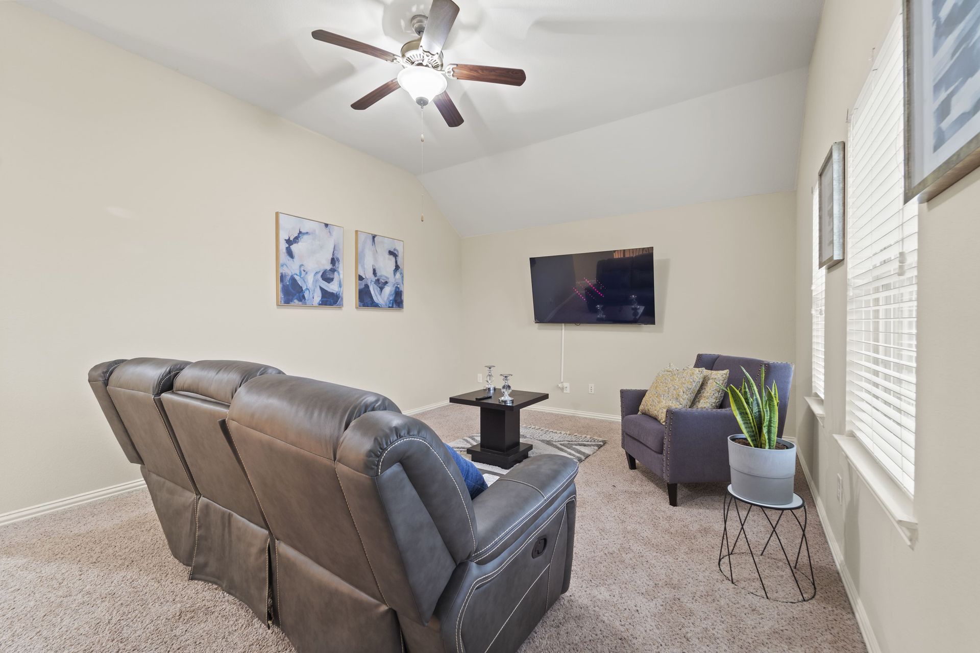 Cozy living room with a reclining couch, armchair, and TV on a light-colored wall.  Art and a plant are visible.