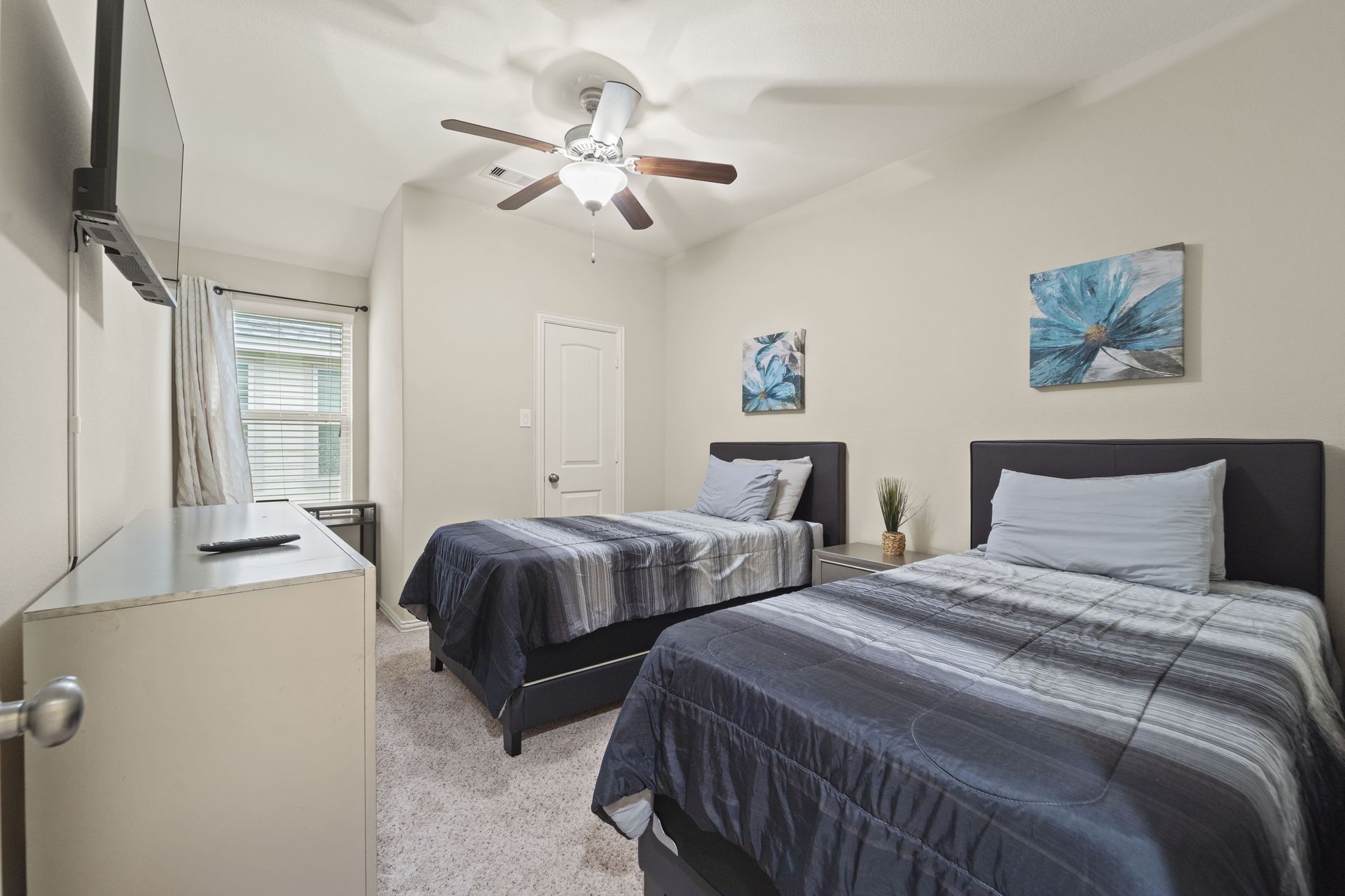 Bedroom with two twin beds, a dresser, a window, and wall art; neutral color palette.