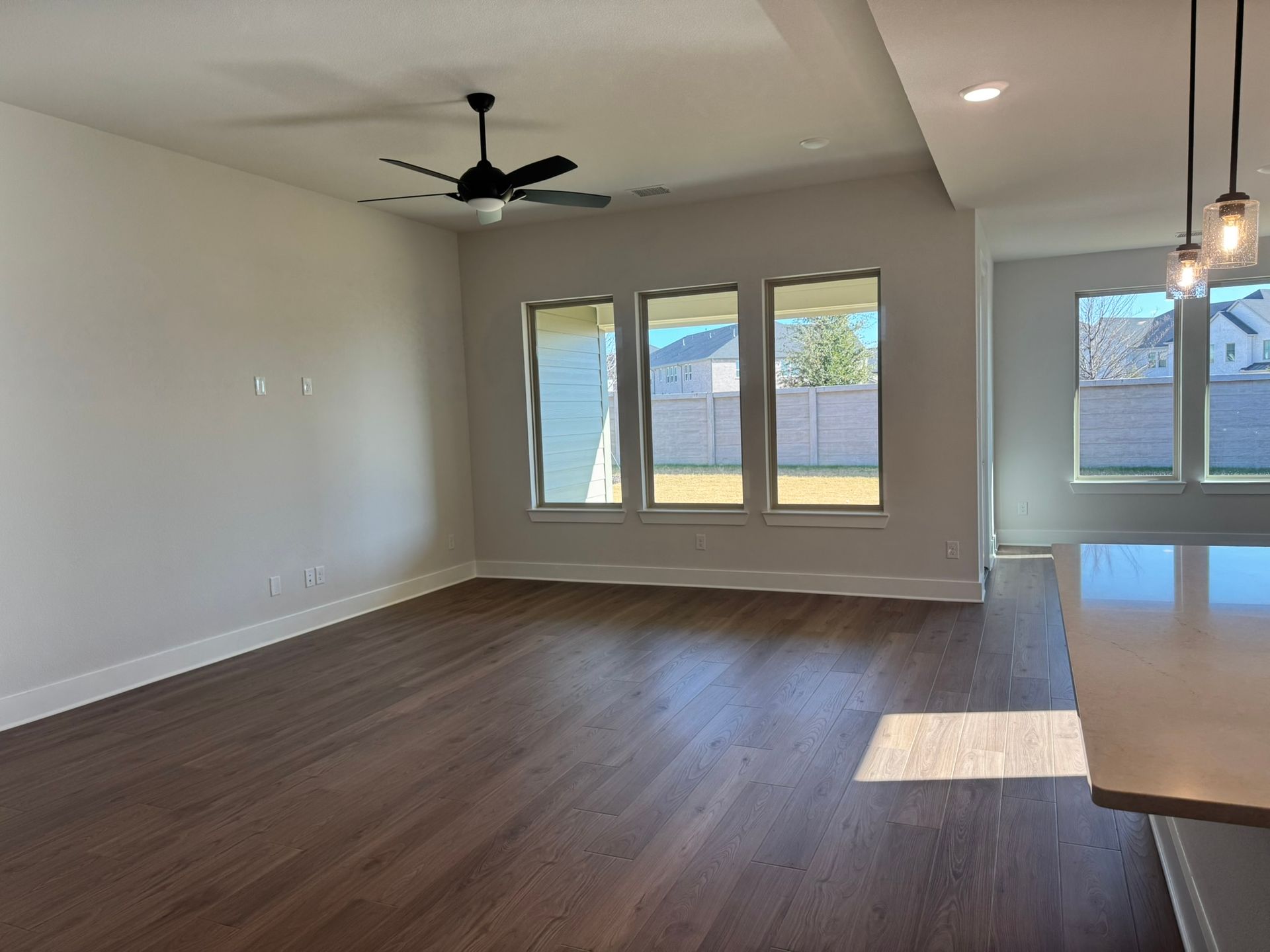 Empty room with gray-brown wood floors, white walls, and a sliding glass door leading to a balcony.