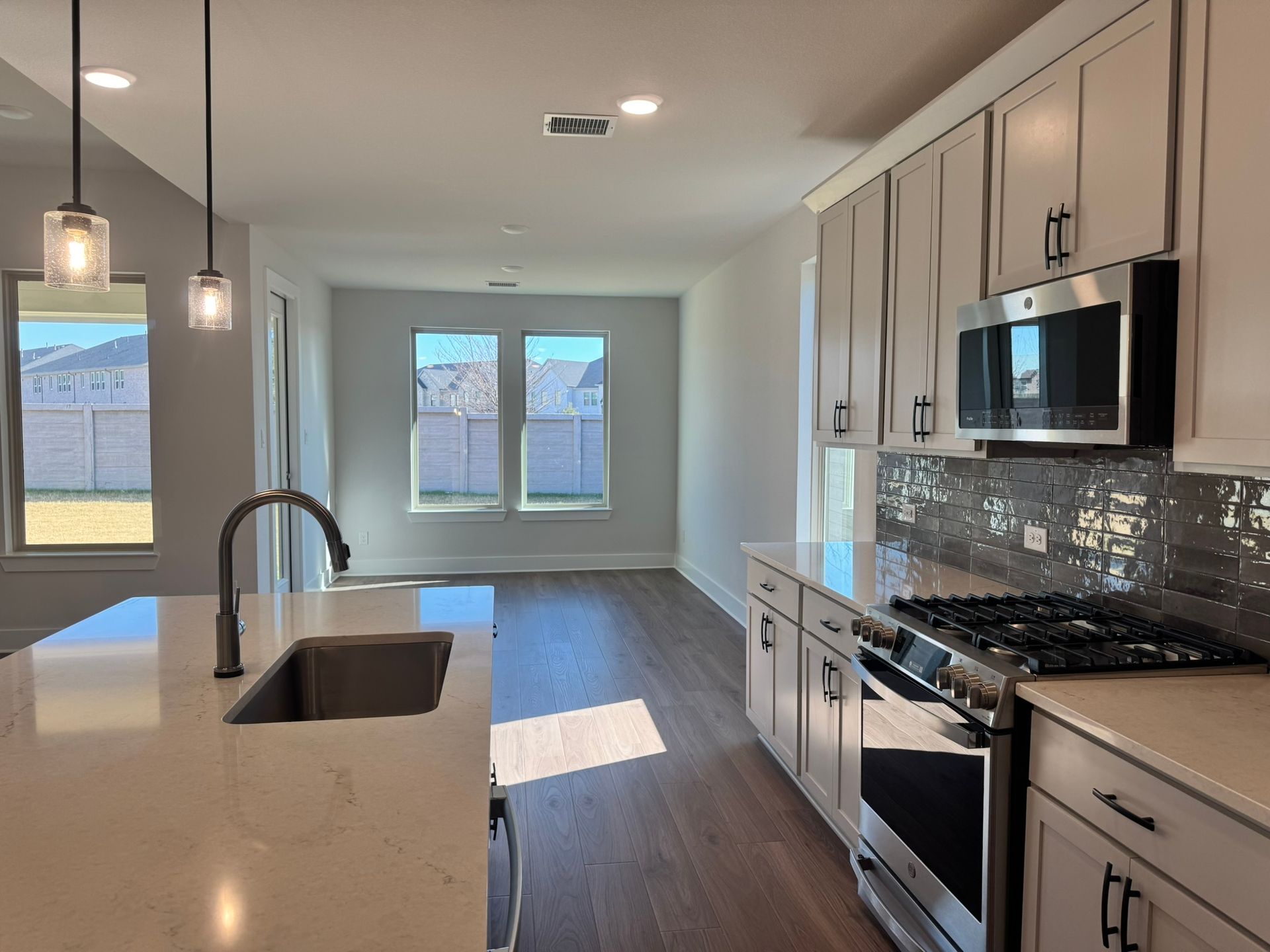 Modern kitchen with light gray cabinets, stainless steel appliances, and dark hardwood floors.