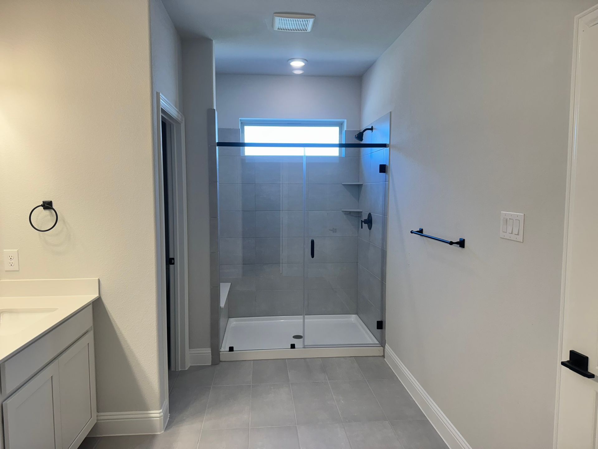 Bathroom with gray tile floor, white walls, glass shower, and black fixtures.