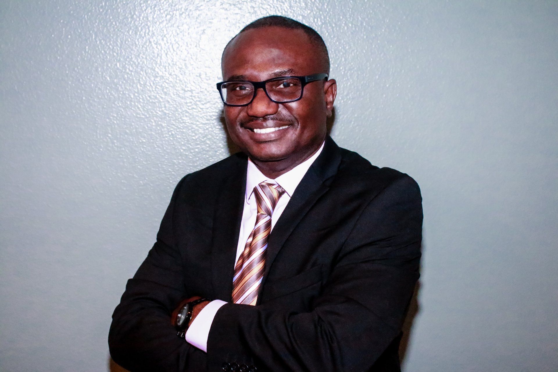 A man in a suit and tie is smiling with his arms crossed.