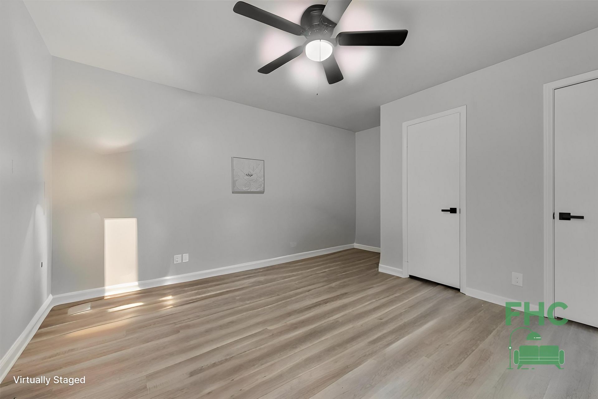 Empty bedroom with light gray walls, wood-look flooring, and white doors. A ceiling fan is mounted.