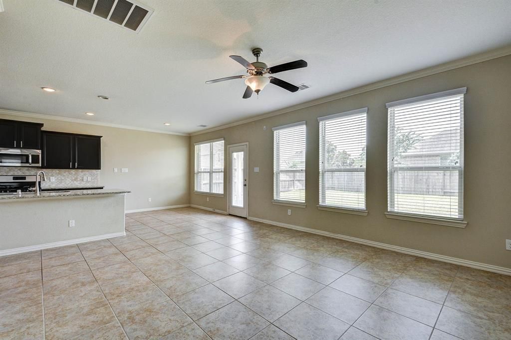 Spacious living area with kitchen and windows, featuring a ceiling fan and beige tile flooring.