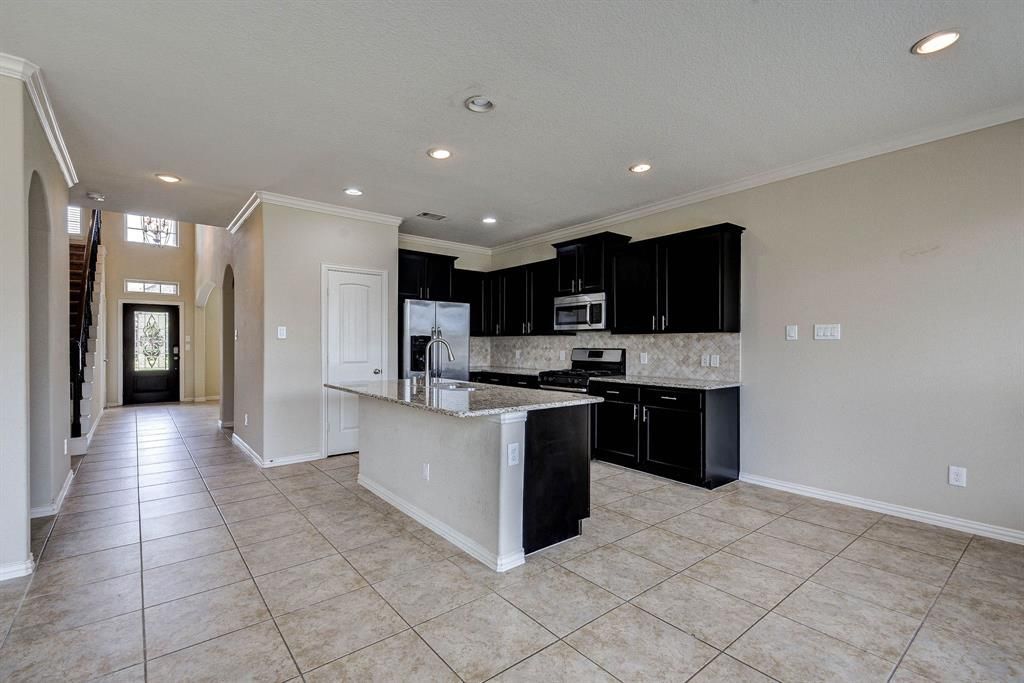 Open-concept kitchen and hallway. Black cabinets, light countertops, and tile floors. Hallway with front door on the left.