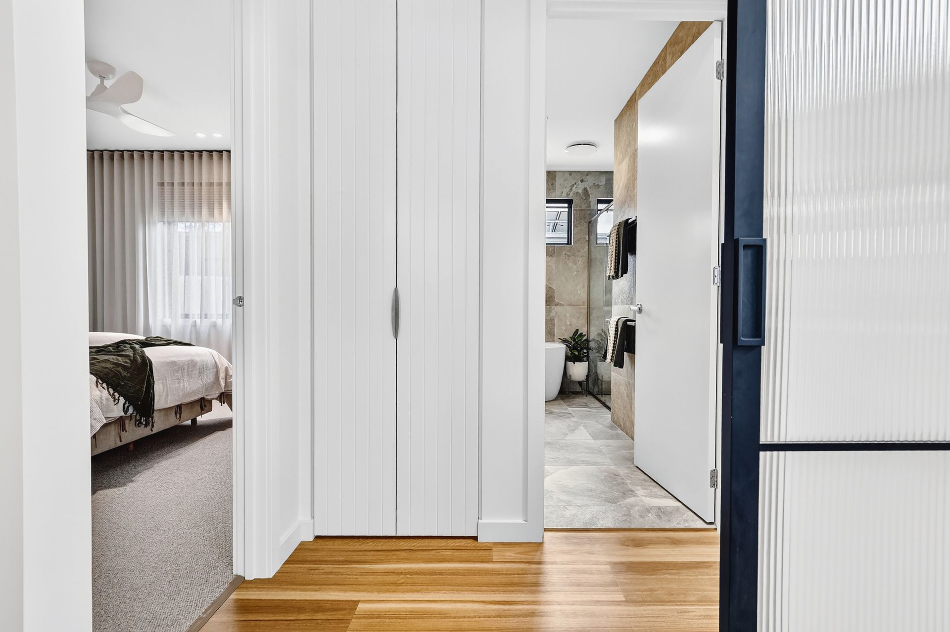 Hallway with bedroom and bathroom entrances; hardwood floors, white doors, and blue door frame.