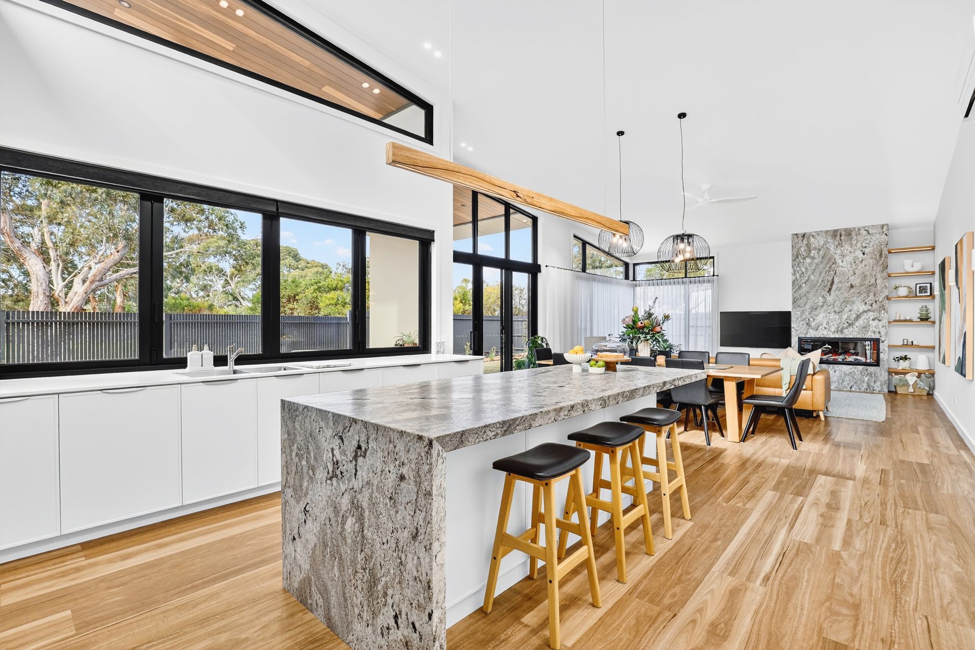 Modern kitchen with island, white cabinets, wood floor, windows, and dining area.