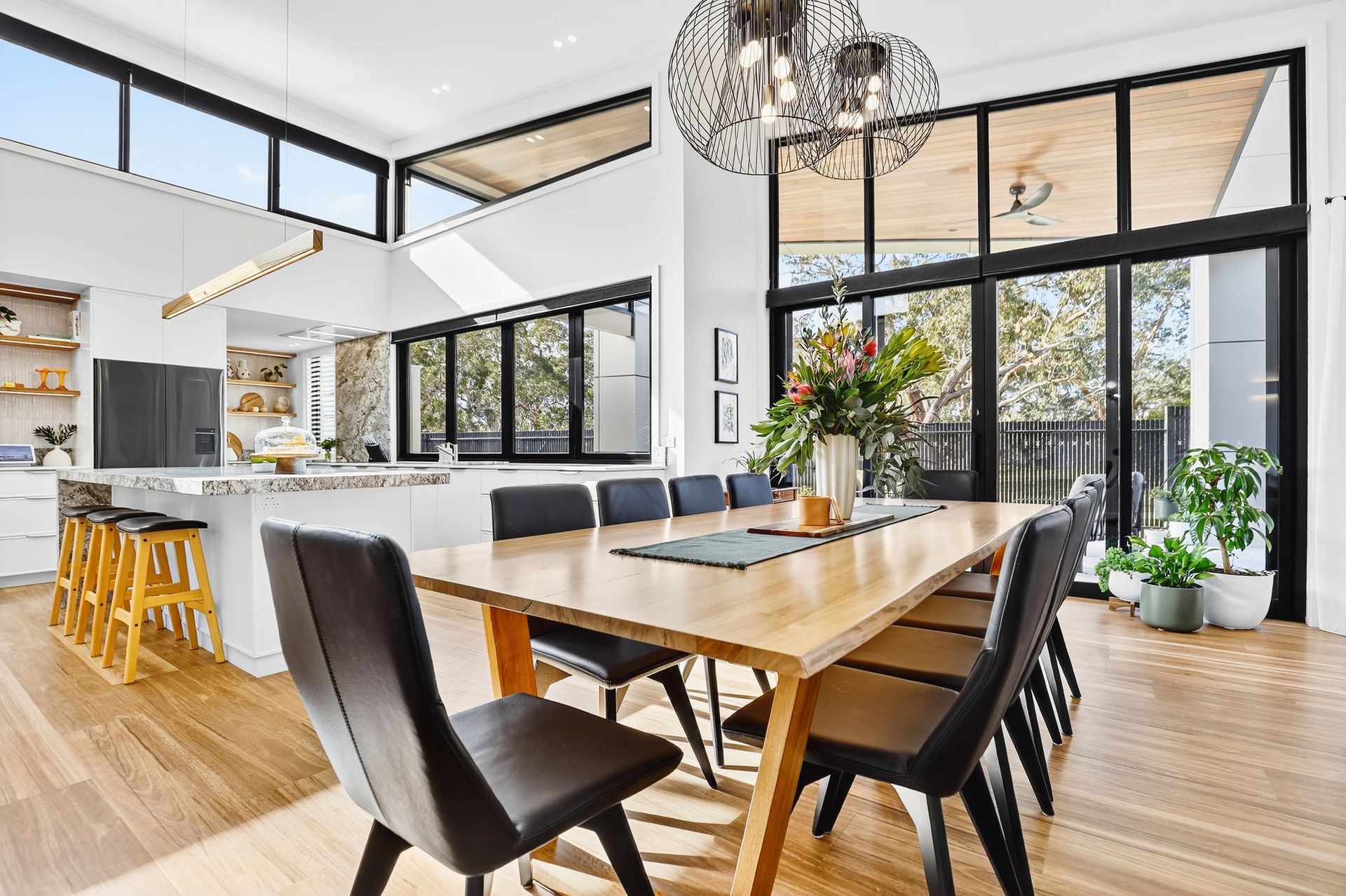 Spacious dining room with large windows, wooden table and chairs, and a kitchen with island.