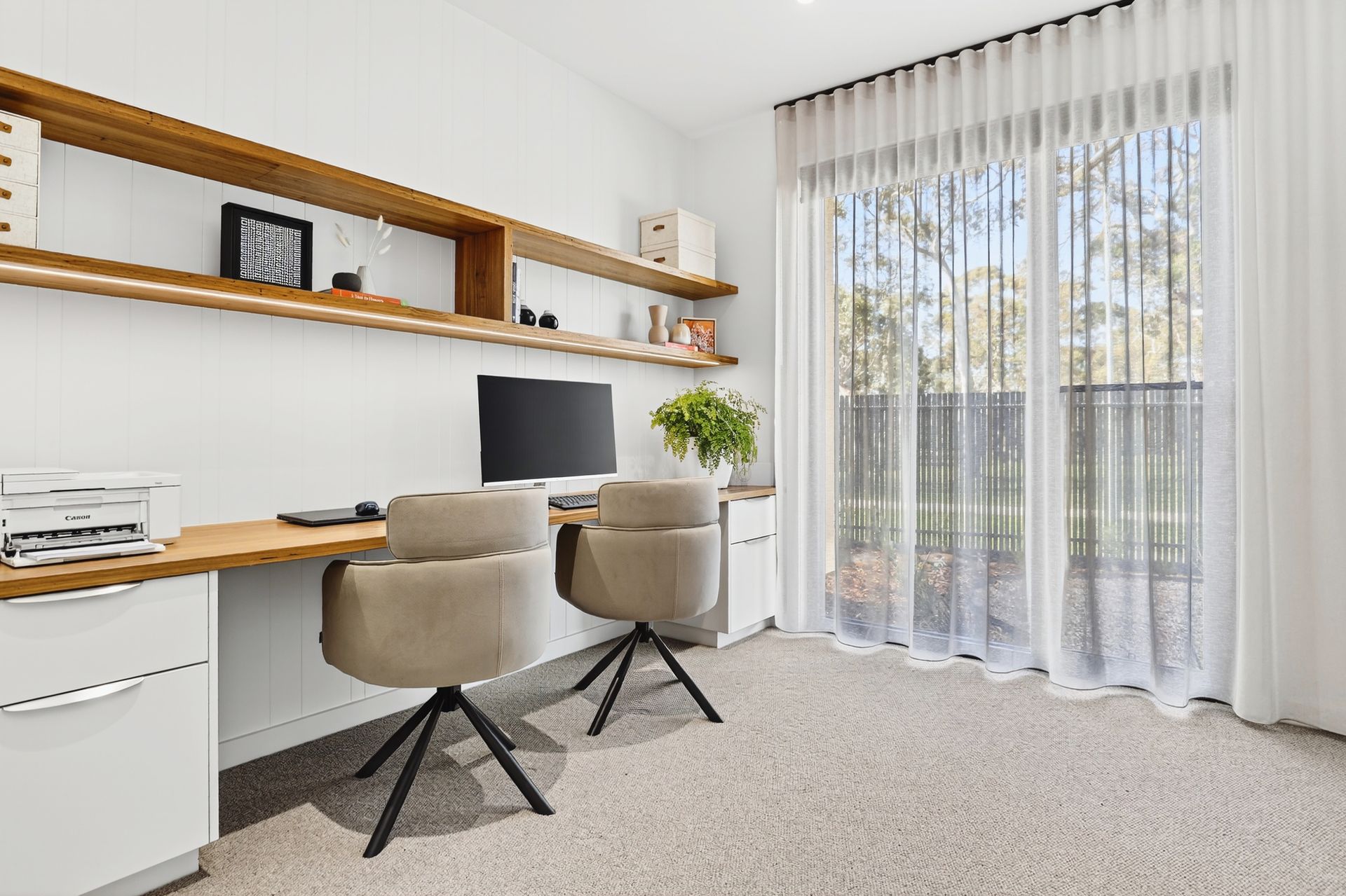 Home office with two desks, tan chairs, and floor-to-ceiling sheer curtains.