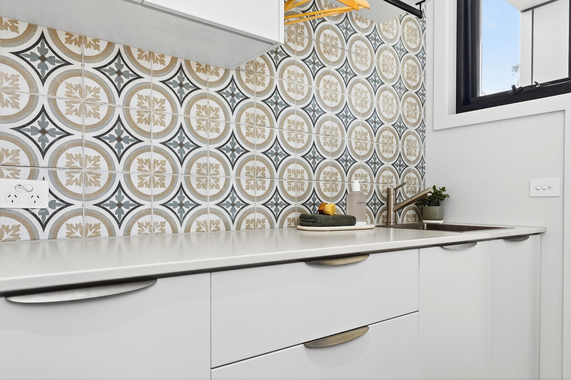 White kitchen with patterned backsplash, countertop, and sink near a window.