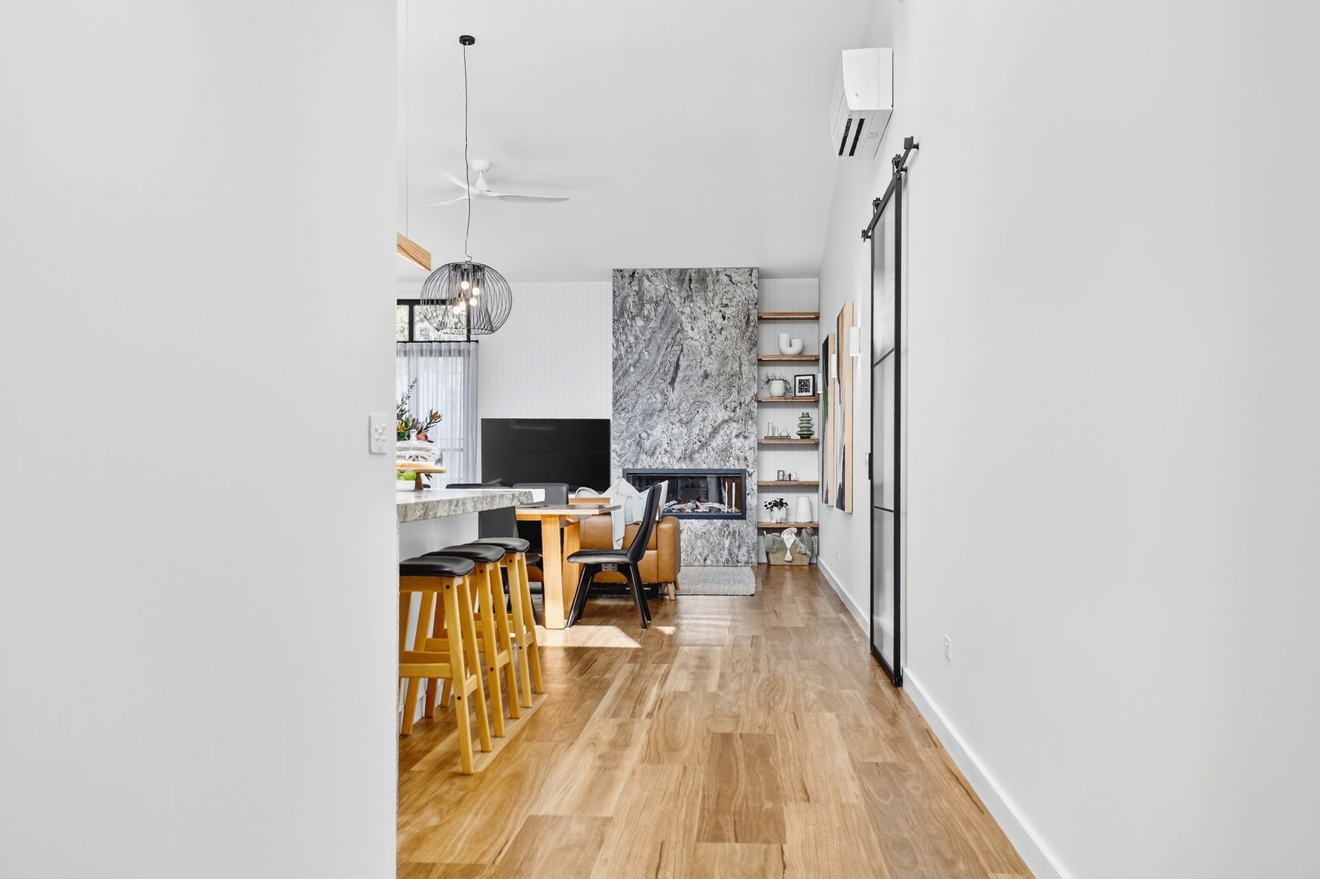 Hallway leading to a living room with fireplace, kitchen island, and wooden floors.