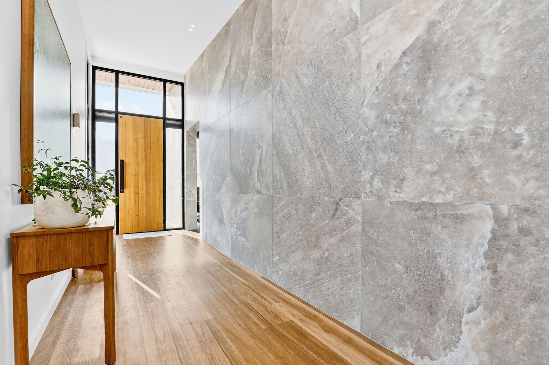 Hallway with wooden floors, stone wall, wooden console, and front door.