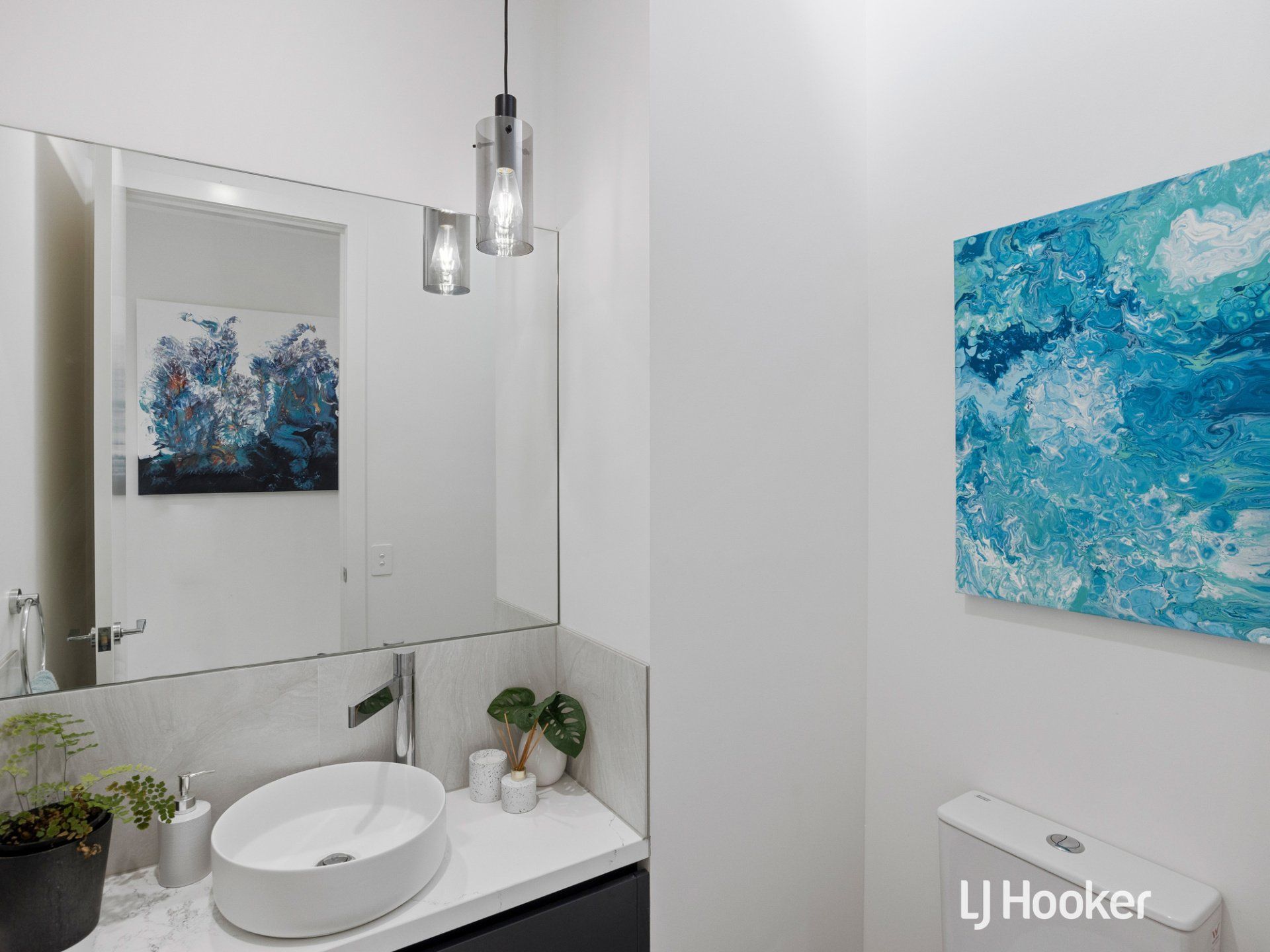 A bathroom with a sink , toilet , mirror and painting on the wall.