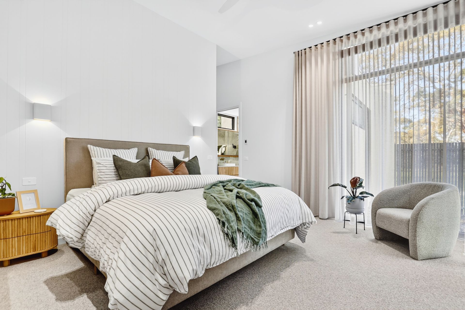 Bedroom with bed, chair, and large window with sheer curtains; neutral tones.