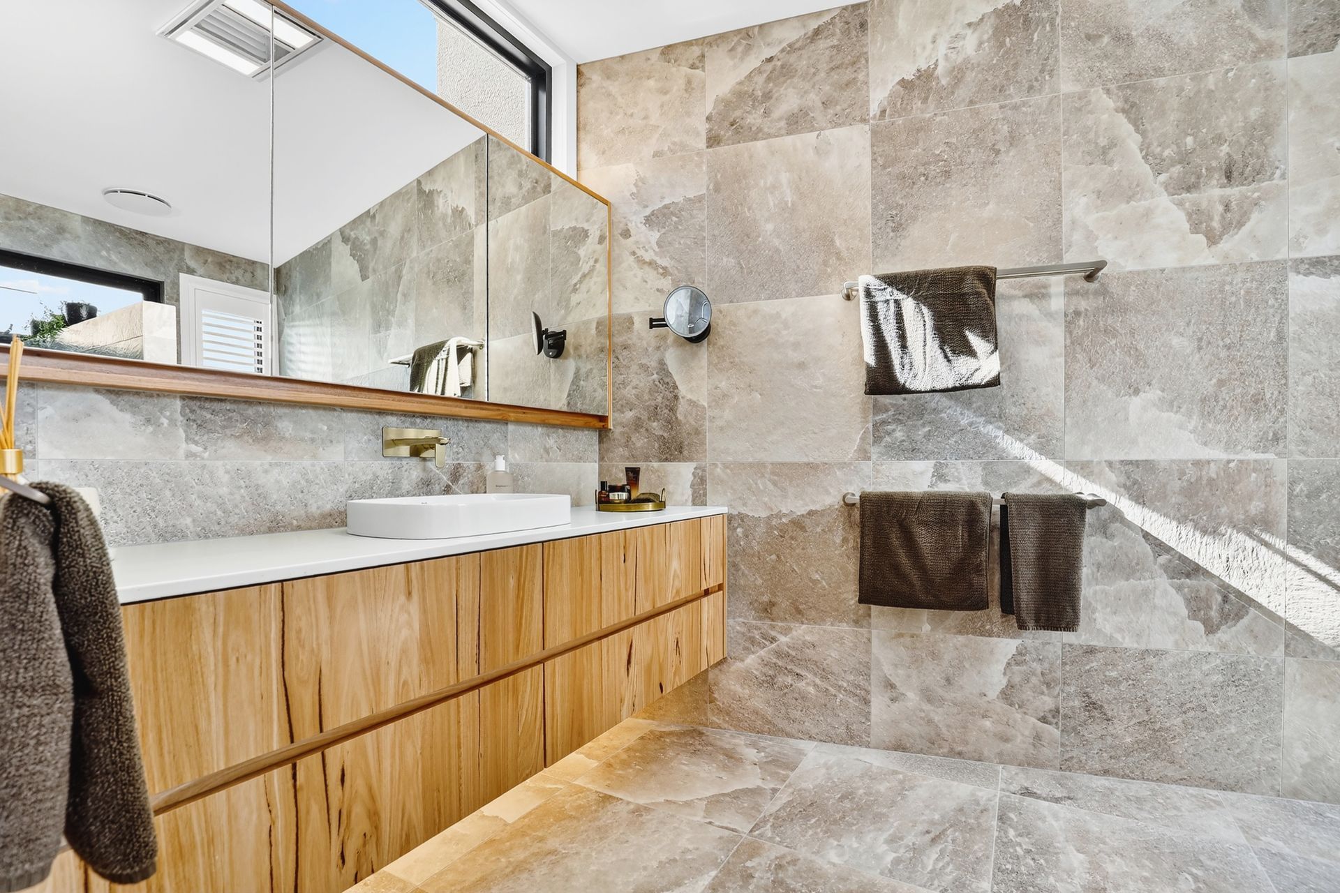 Modern bathroom with gray tiled walls, light wood vanity, and white sink.