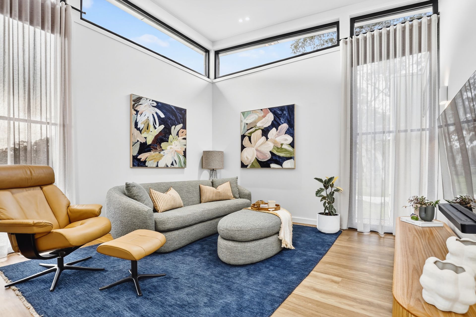 Living room with blue rug, gray sofa, leather chair, and floral art.