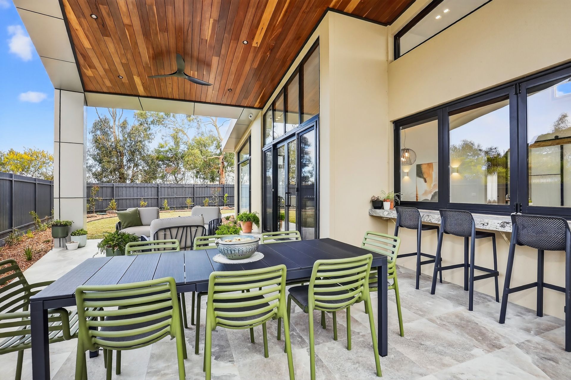 Outdoor dining area with a black table, green chairs, and a bar with stools.