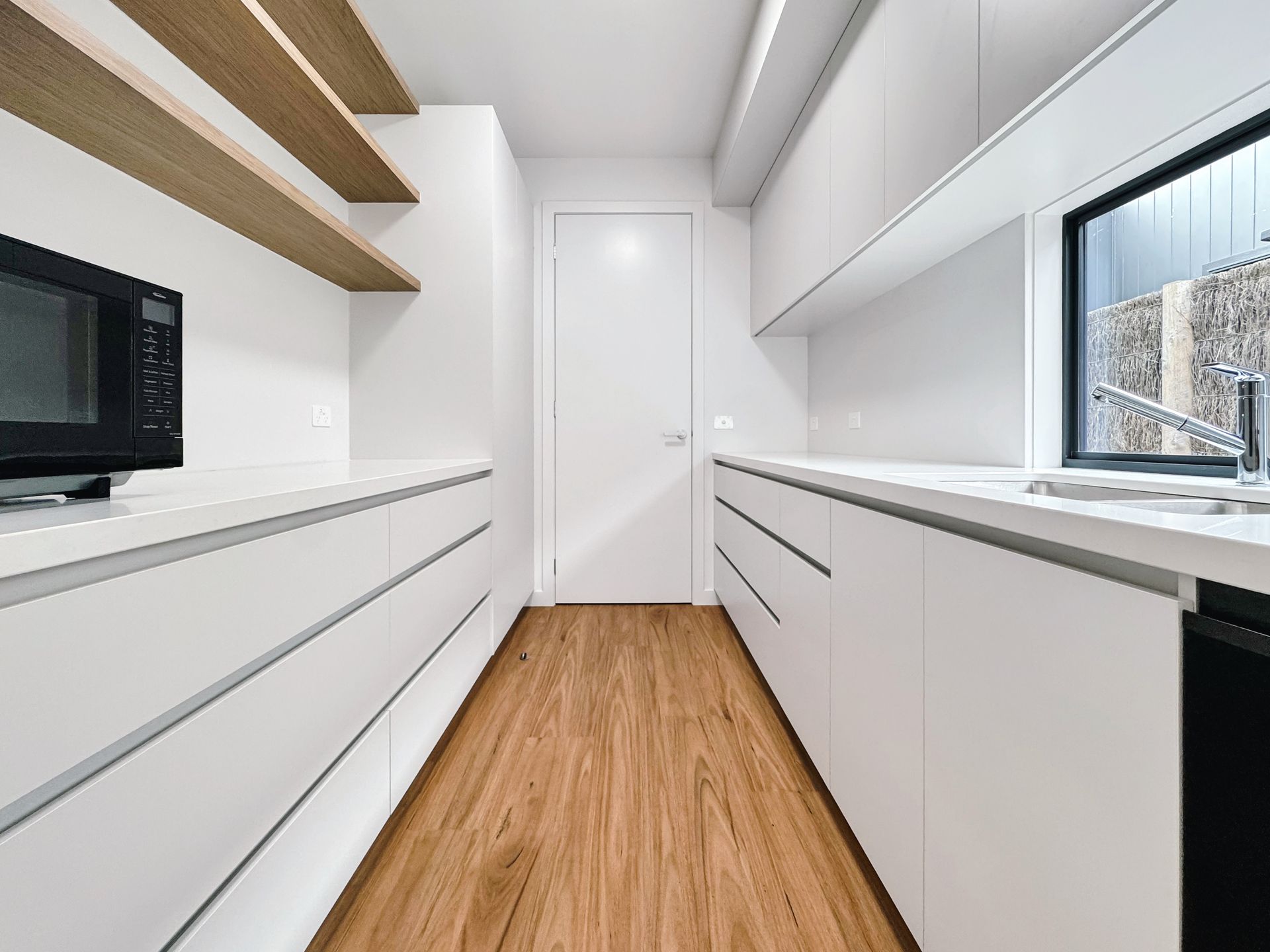 A kitchen with white cabinets , wooden floors , a sink , and a microwave.