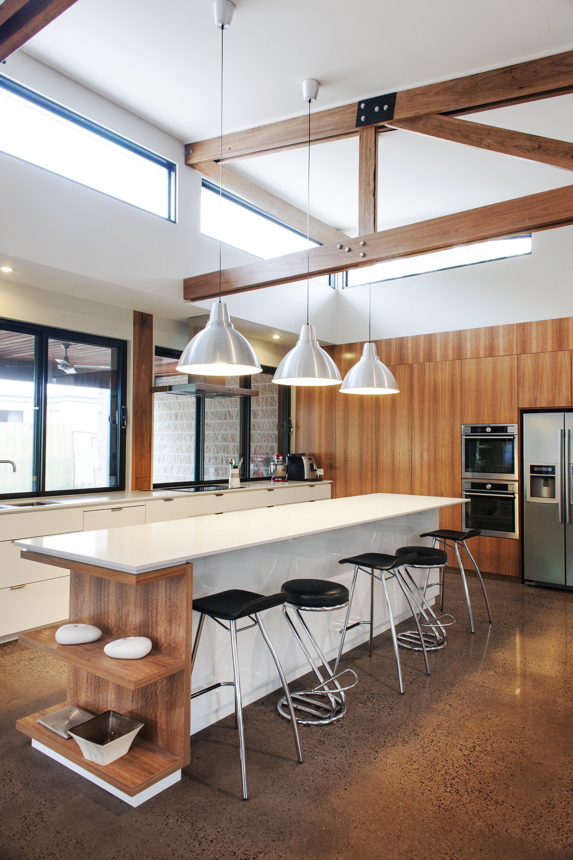 A kitchen with a long island , stools and a refrigerator.