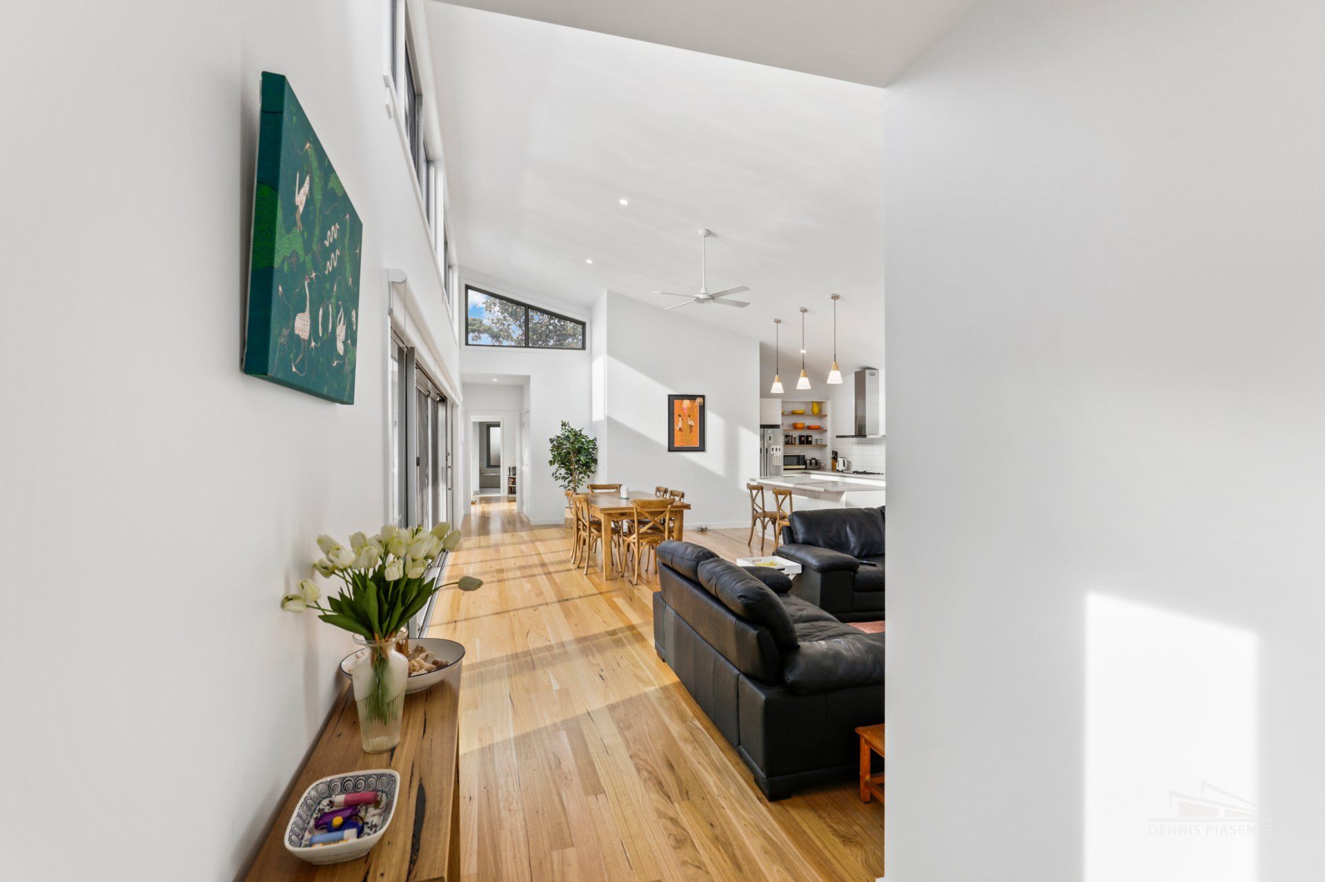 A living room with hardwood floors , a couch , a table and a painting on the wall.