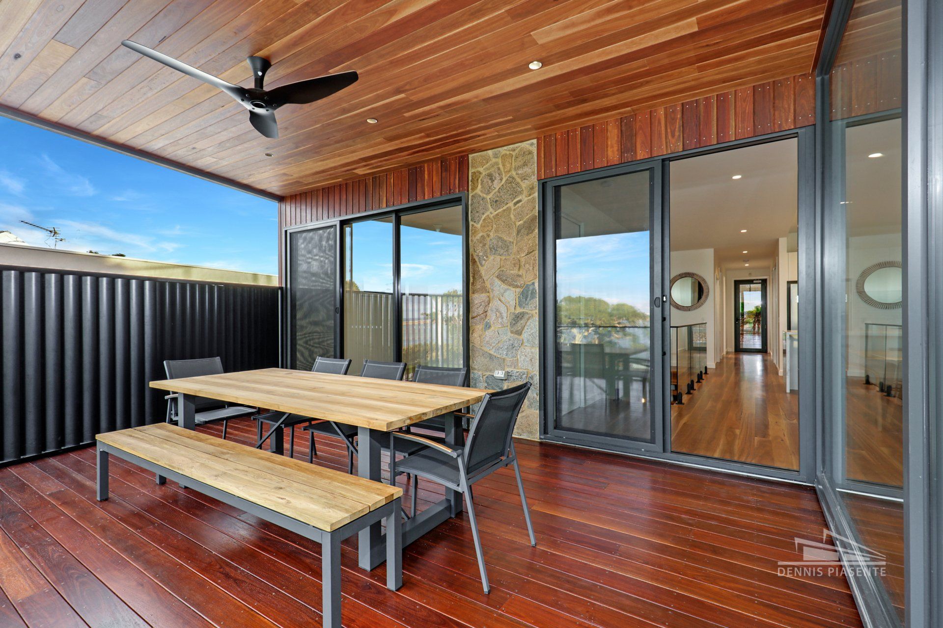A wooden deck with a table and chairs and a ceiling fan.