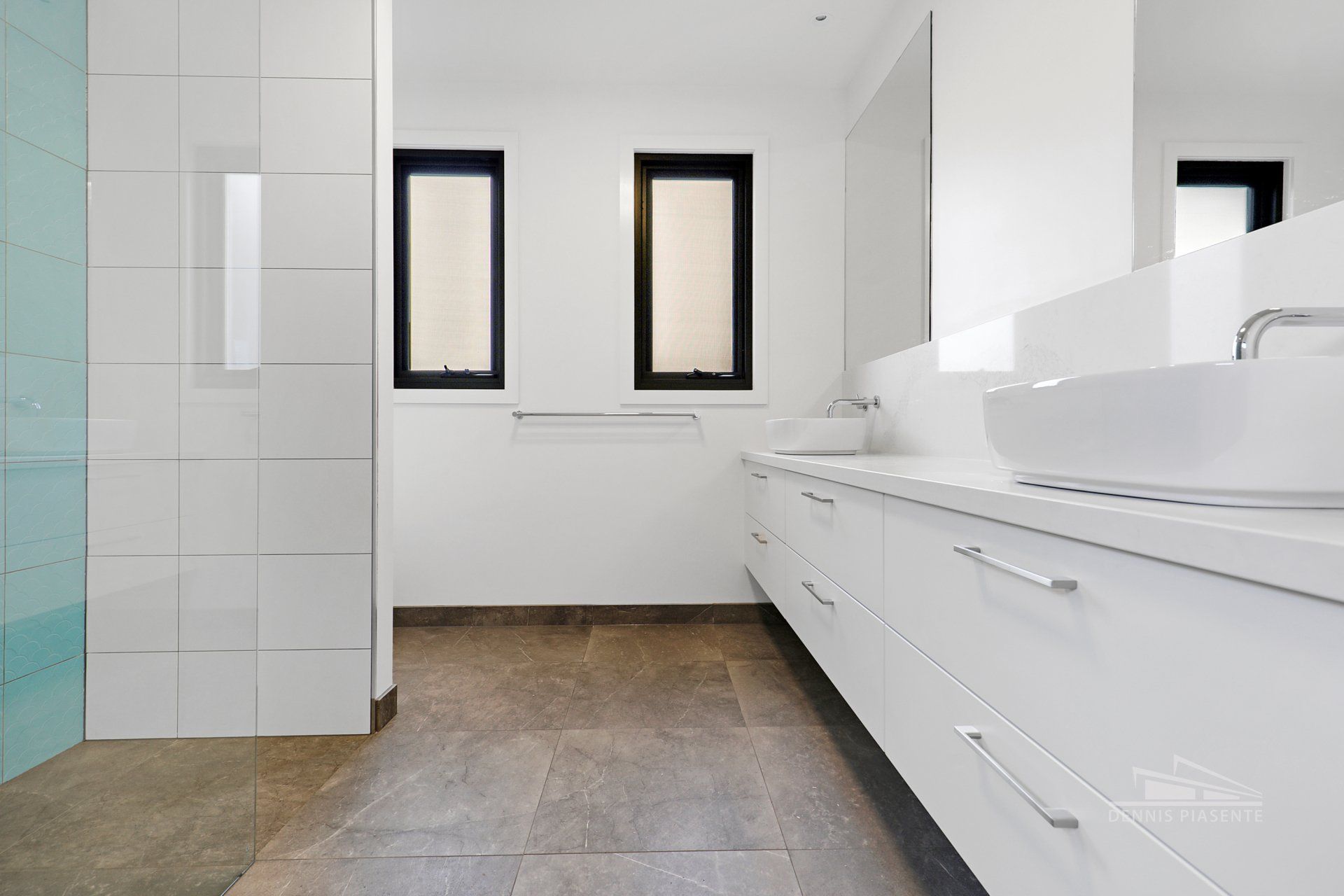 A bathroom with white cabinets , a sink , a mirror and a walk in shower.