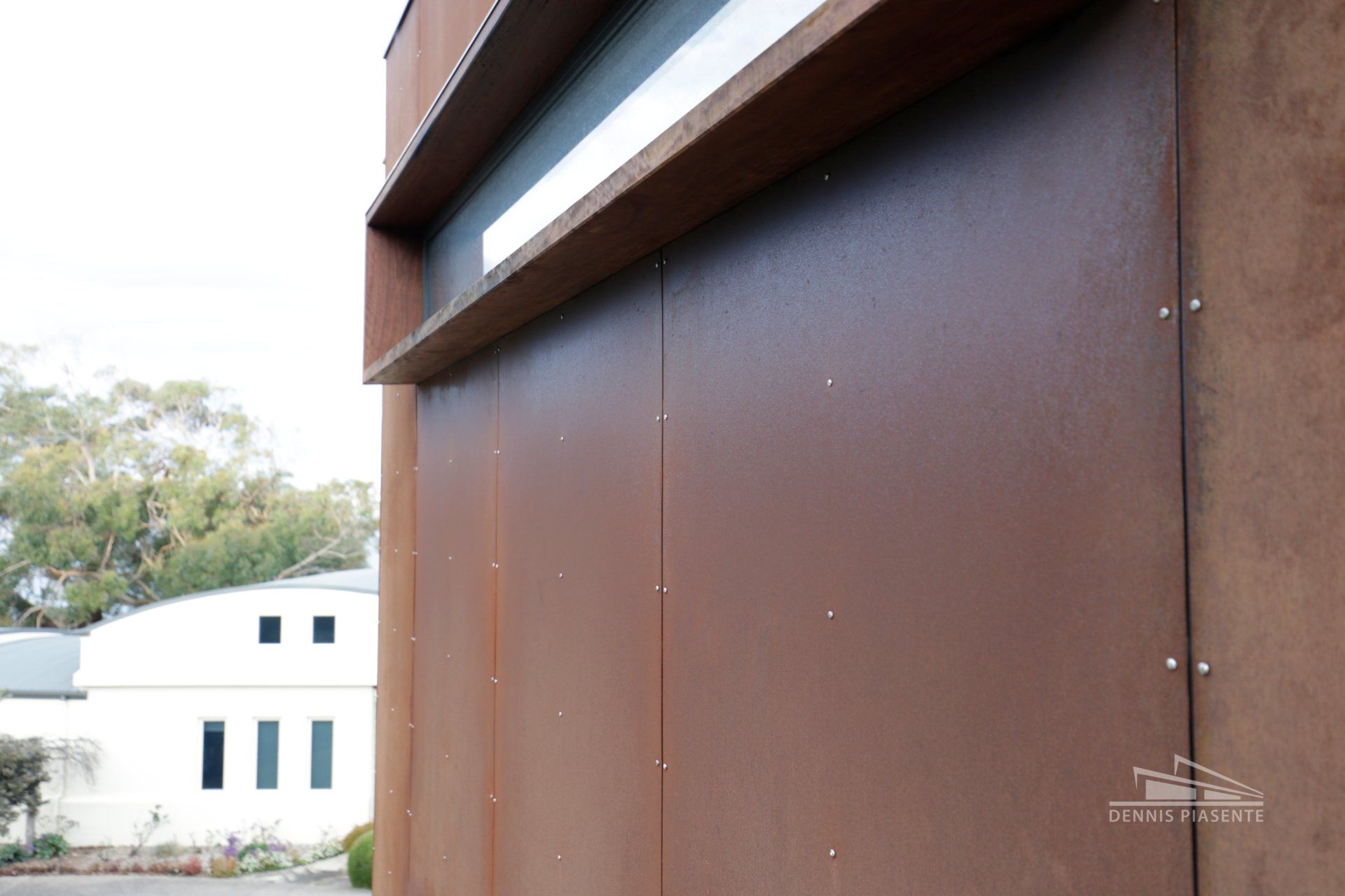 A close up of a brown wall with a white building in the background.