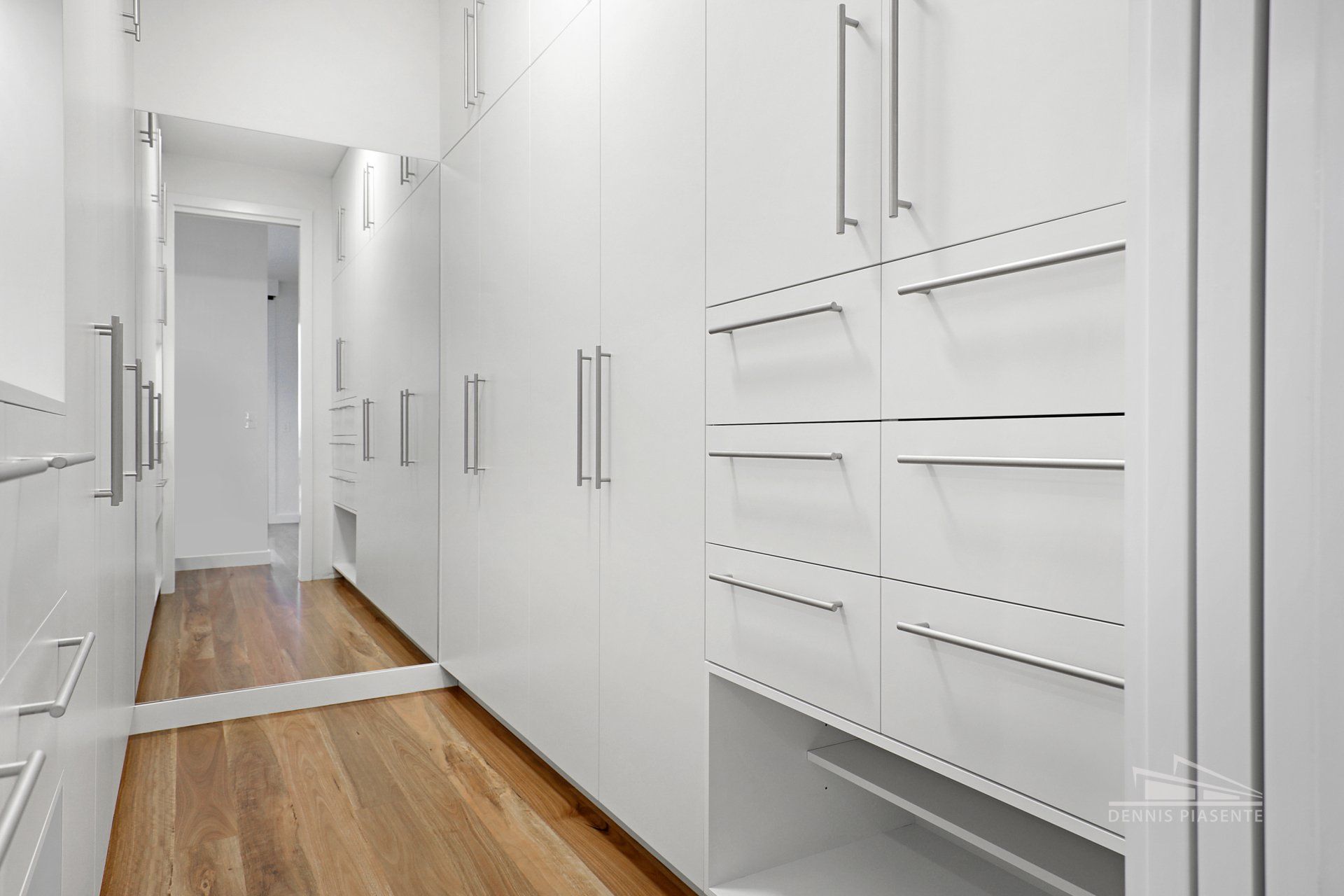 A walk in closet with white cabinets and drawers and a large mirror.
