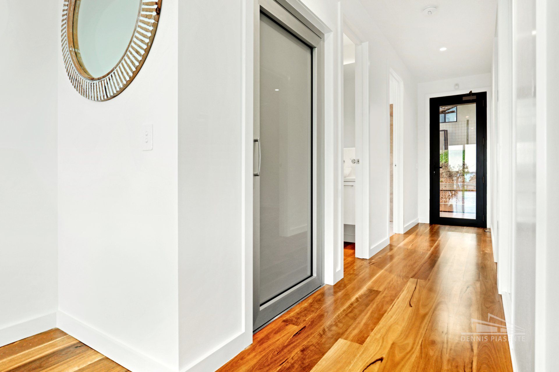 A hallway with hardwood floors and a mirror on the wall.