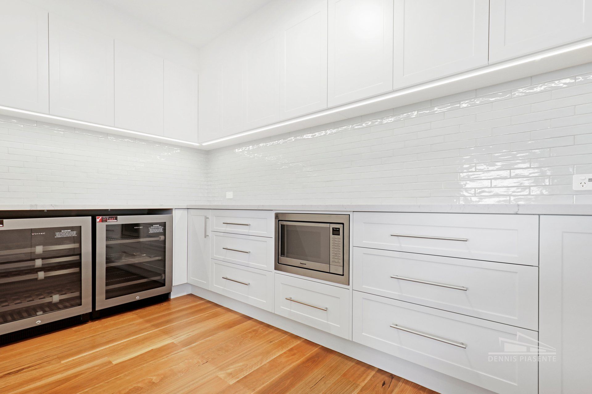 A kitchen with white cabinets , wooden floors , stainless steel appliances and a wine cooler.