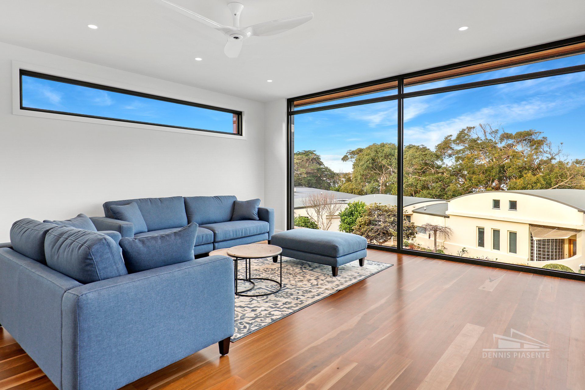 A living room with a blue couch , two chairs , a coffee table and a large window.