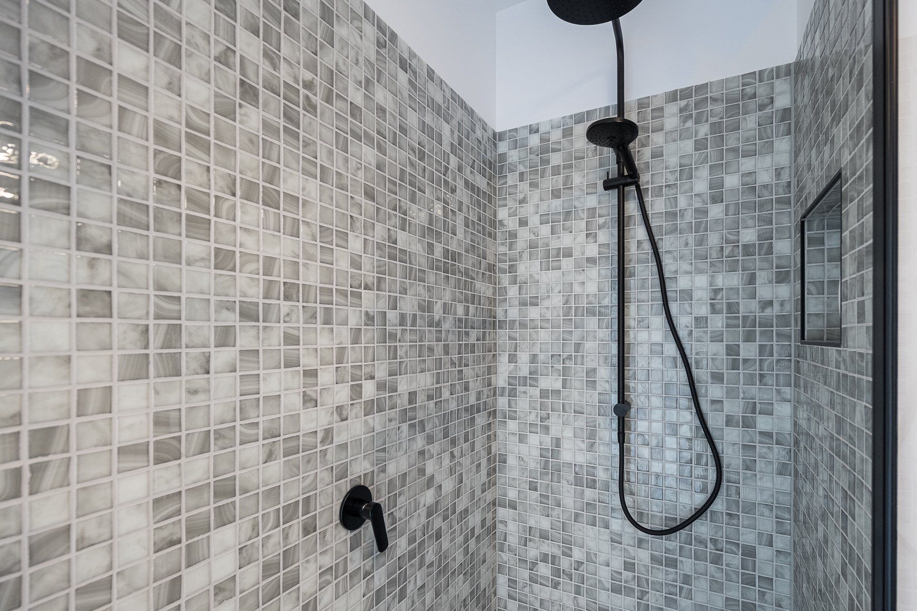 A shower with a black shower head and a mosaic tile wall.