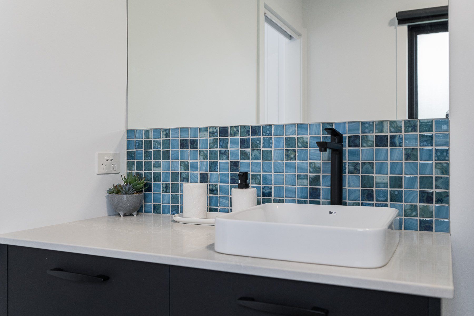 A bathroom with a sink , mirror and blue tiles