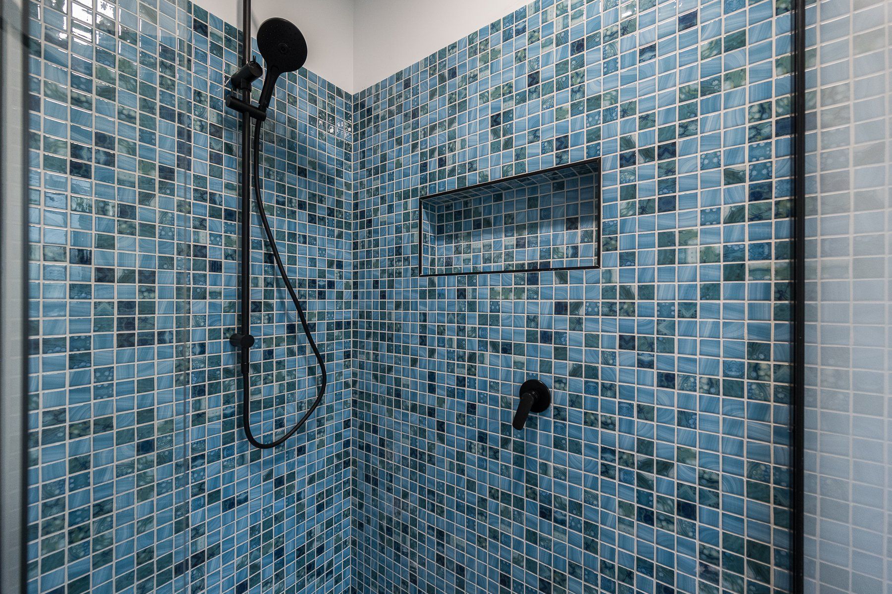 A shower with blue tiles and a black shower head.