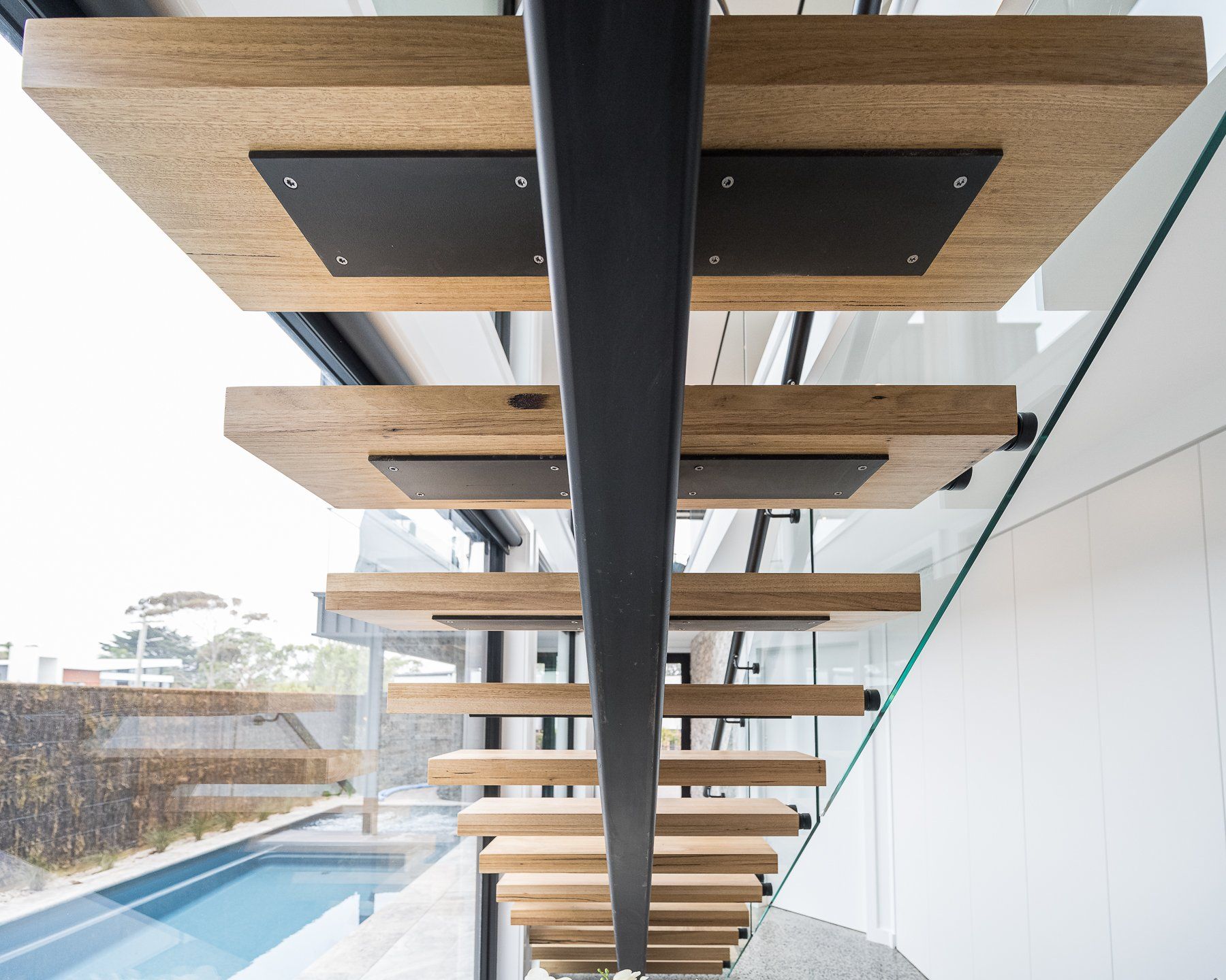 A wooden staircase with a black railing and a pool in the background
