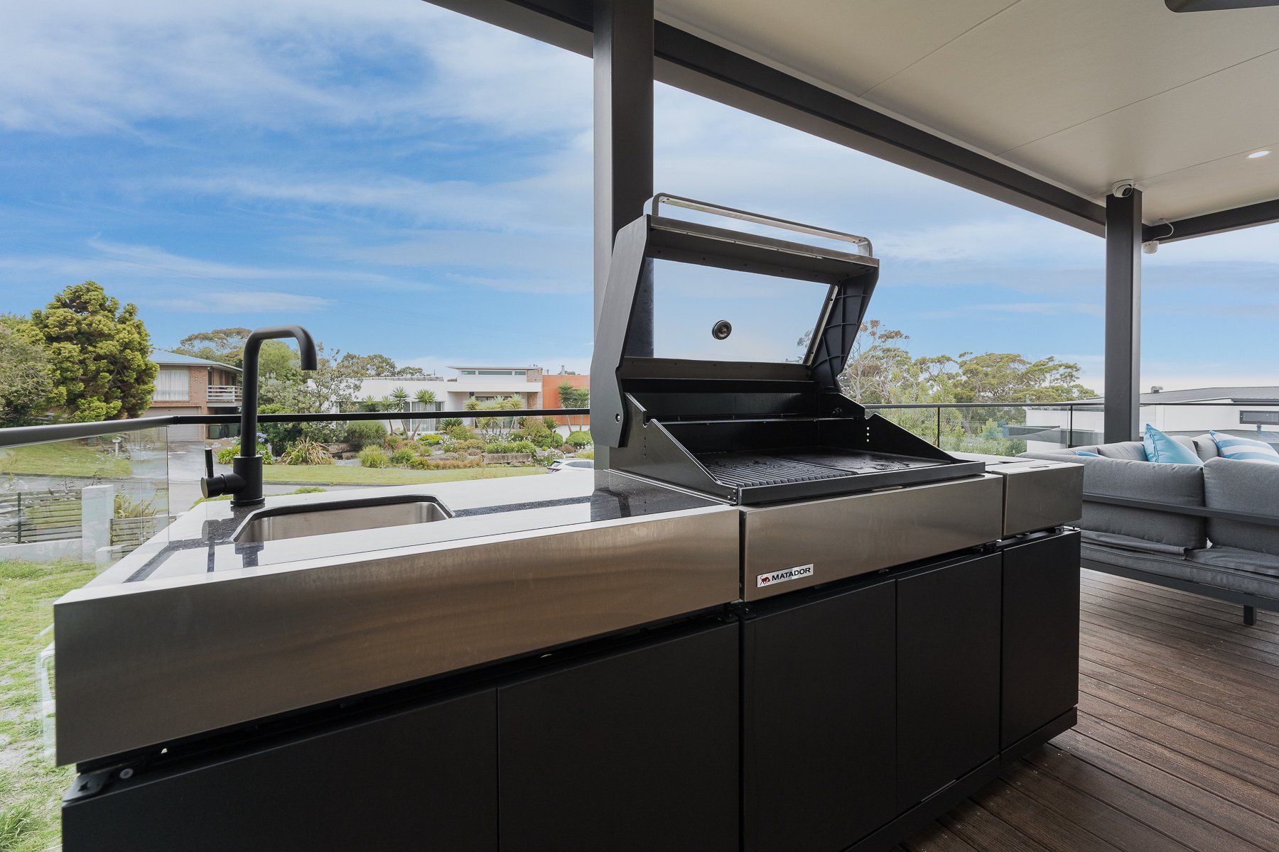 A large outdoor kitchen with a grill and sink on a deck.