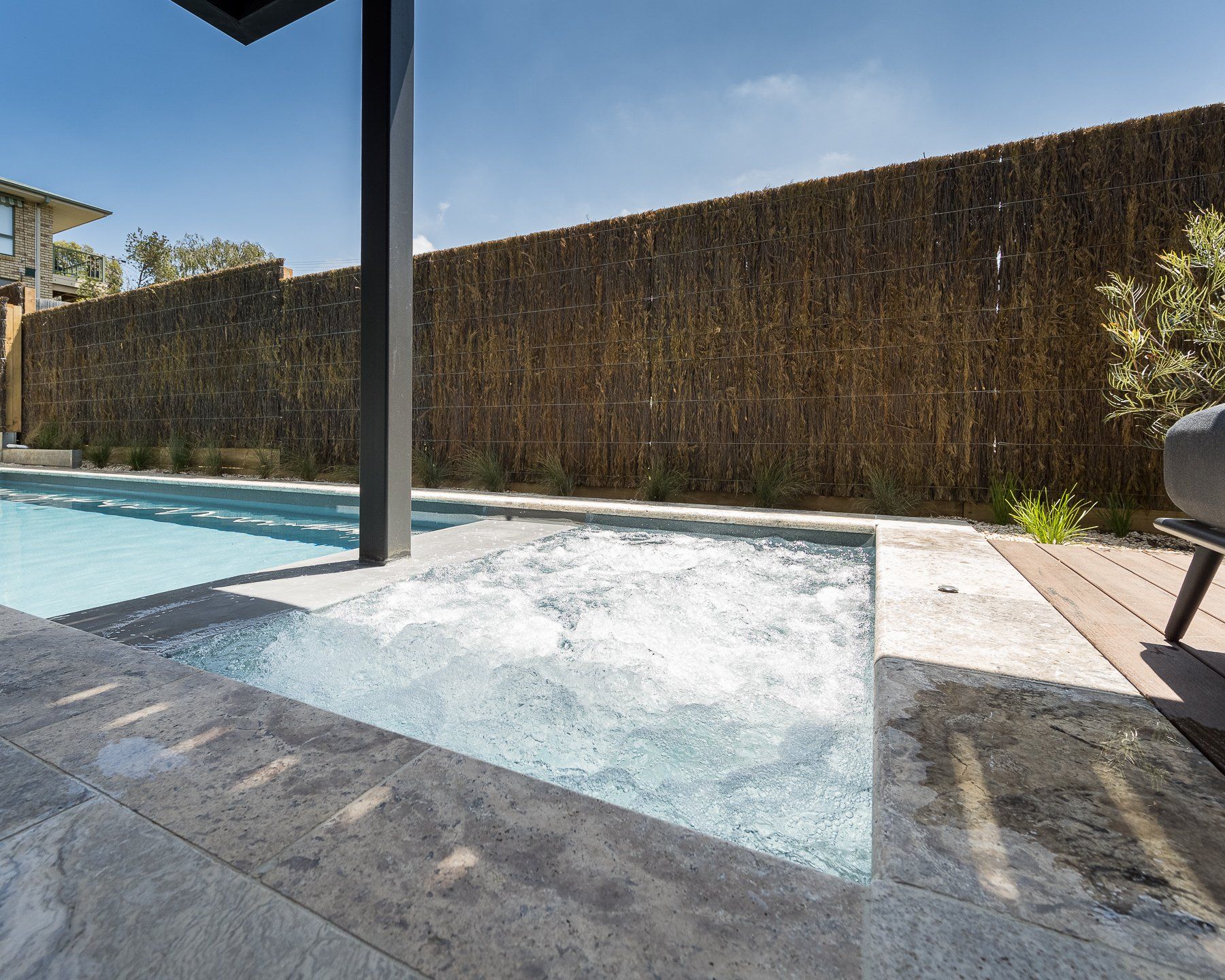 A large swimming pool is surrounded by a fence and a chair.