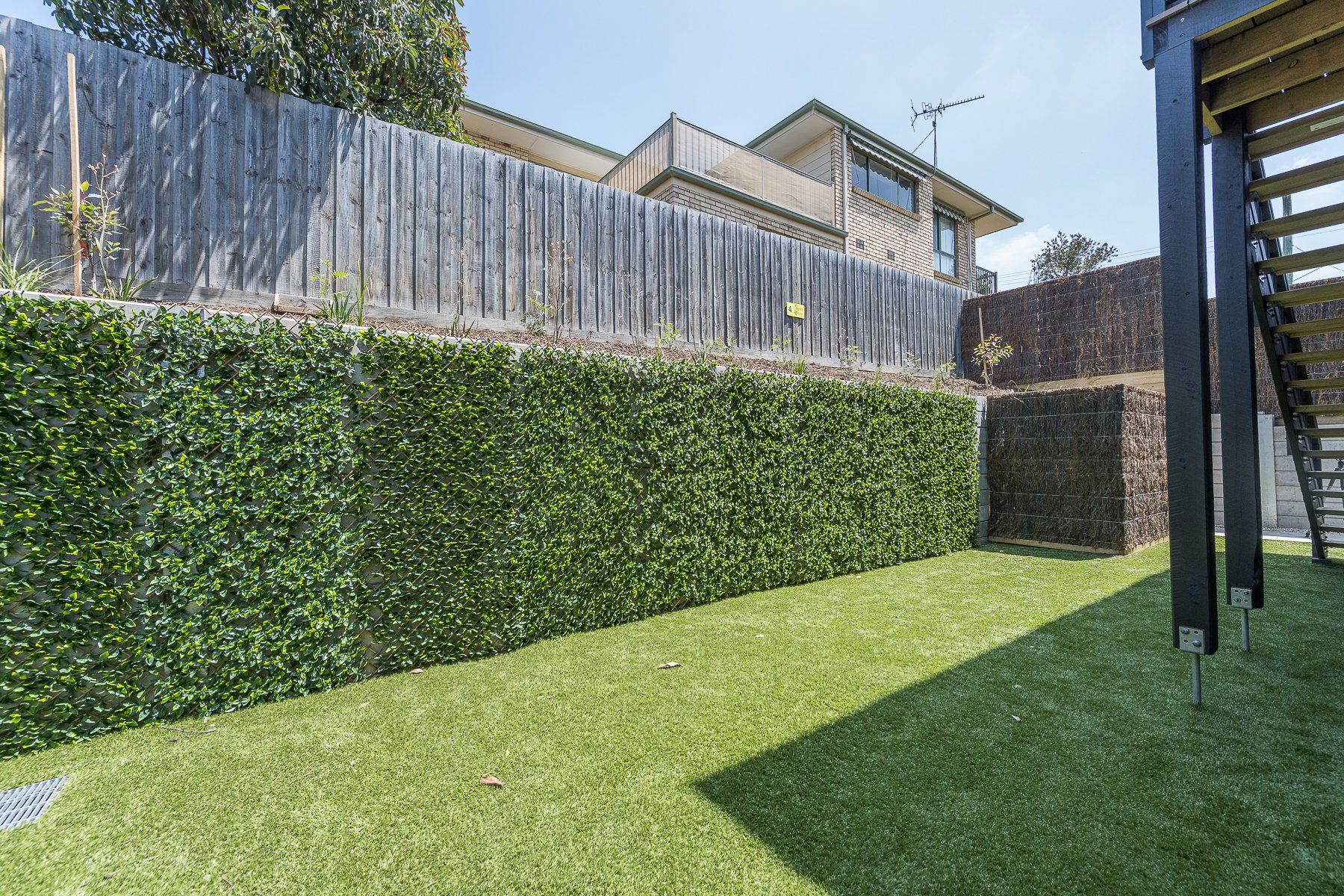 A backyard with a fence , stairs and a hedge.