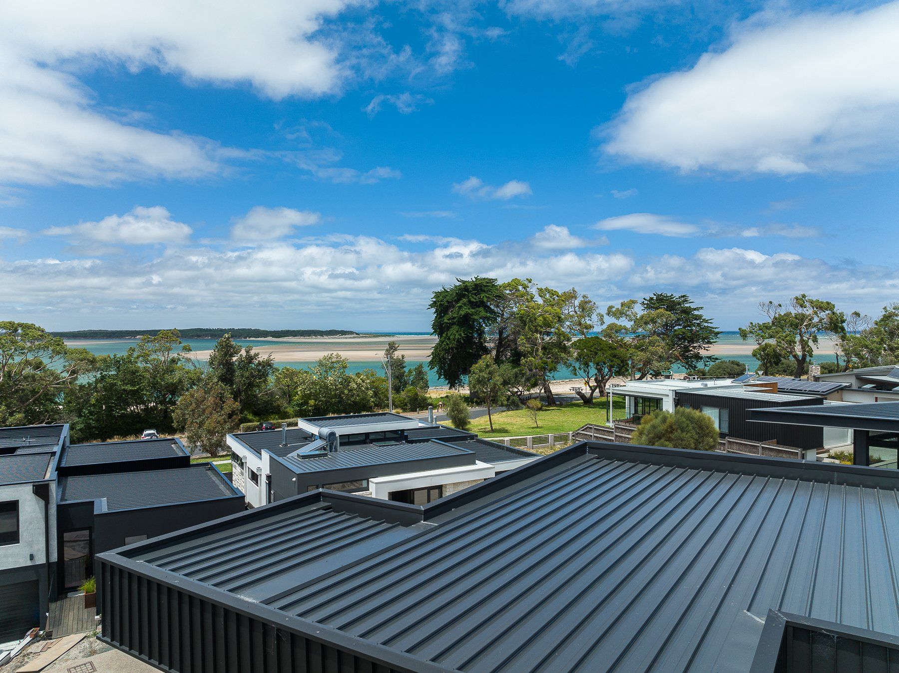 An aerial view of a house with a black roof and a view of the ocean.