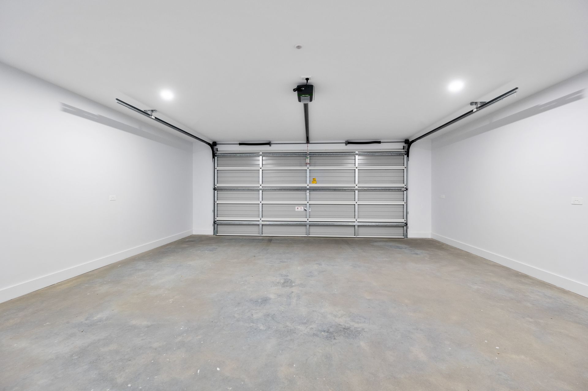 Empty, modern garage with a closed, silver garage door, white walls, and a gray concrete floor.