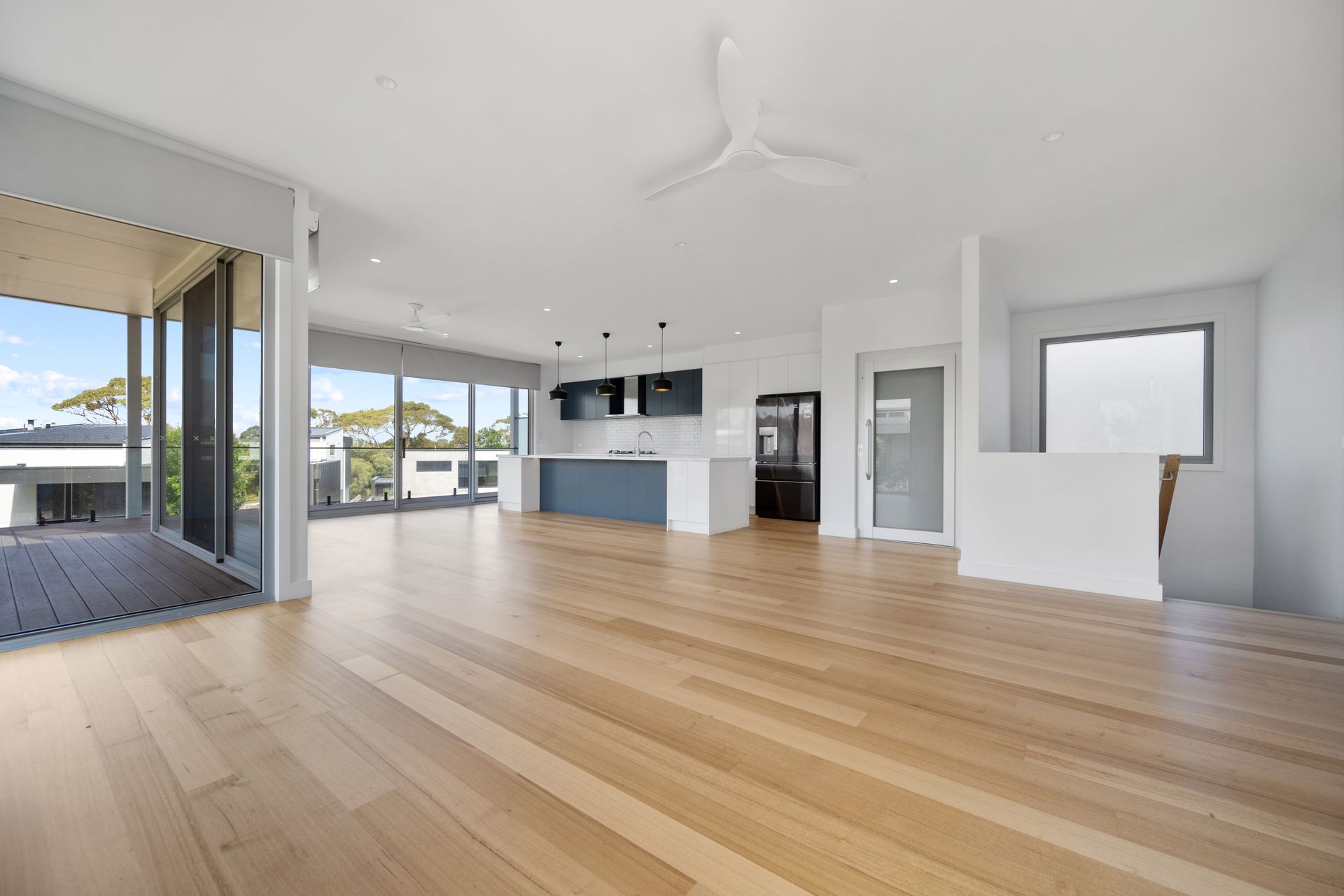 Empty open-plan living space with hardwood floors, modern kitchen, and glass doors leading to a deck.